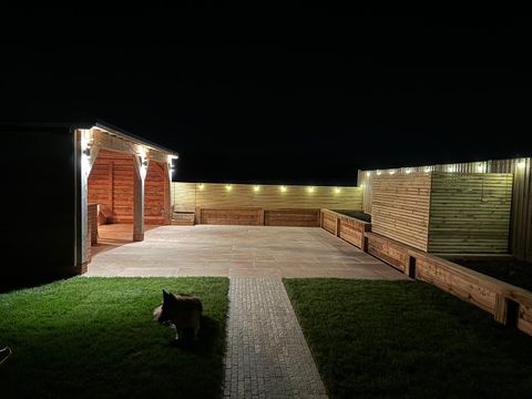 Completed timber garden building and patio lit by garden lighting at night